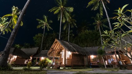 Zooming out timelapse of picturesque woonden indonesian houses with straw roofs and palms under wonderful sky with million bright stars. Gili Air island - Powered by Adobe
