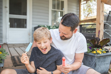 father and son enjoying frozen treat on a porch
