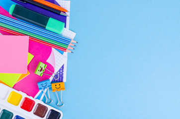 Back to school with schools accessories - paints, pencils, notebooks, scissors, markers, blue background. 