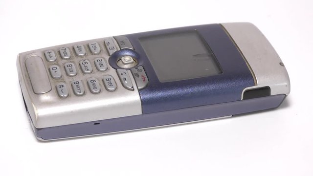 A blue and silver old phone rotating on white surface
