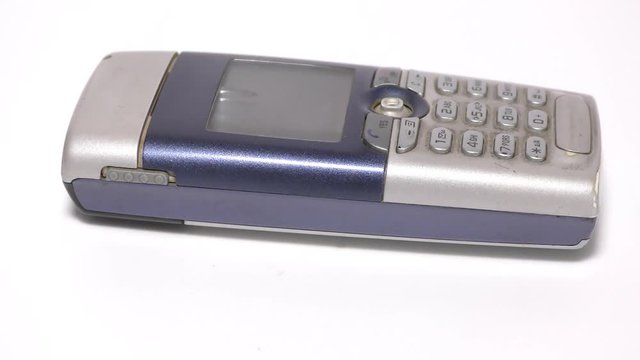 An old mobile phone with display screen and on white base moving