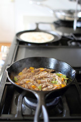 Mexican style pulled pork, known as carnitas, cooking in a cast iron skillet with a flour tortilla on a camal skillet.