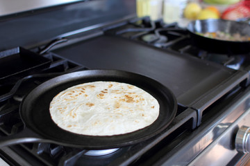 Tortilla baking on a camal skillet on the stove top.