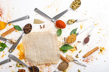 Various spices ( cumin, coriander, curry, paprika, chili, turmeric cinnamon, fenugreek, cardamom, basil leaf, parsley, cloves )  in  spoons on white background. Top view with copy space.