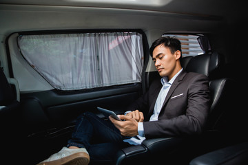 asian young businessman with tablet sitting on passenger seat of his luxury car