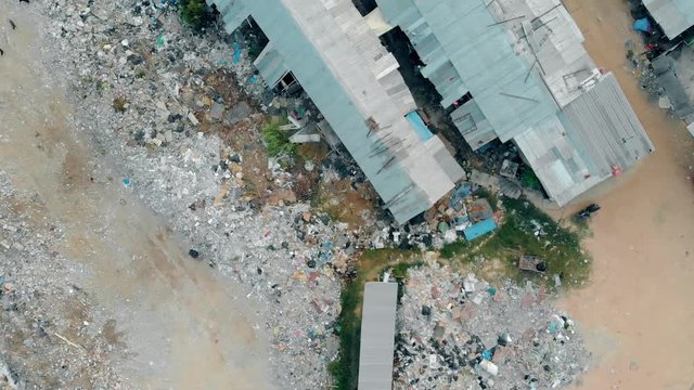 old broken buildings and houses in slums with trash and construction debris against green trees bird eye view