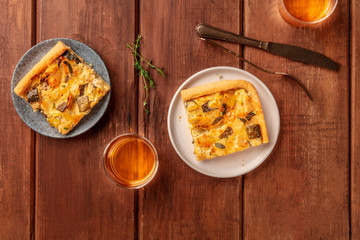 Slices of a zucchini and goat cheese pie with thyme, shot from above on a dark rustic wooden background with white wine