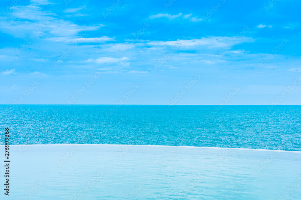 Wall mural Beautiful outdoor infinity swimming pool in hotel resort with sea ocean view and white cloud blue sky