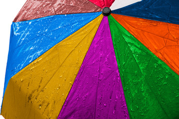 Wet multicolored umbrella close up image on isolated background. Waterproof fabric cloth with water drops and splashes. Rainbow vivid colors. Good or bad weather concept. Rain in four seasons
