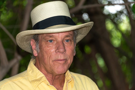 Portrait Of Good Looking Senior Man In His 60s Outdoors In Backyard, Wearing Hat And Yellow Shirt.  Looking Away From Camera