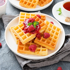 Traditional belgian waffles with fresh raspberry and jam on gray background.