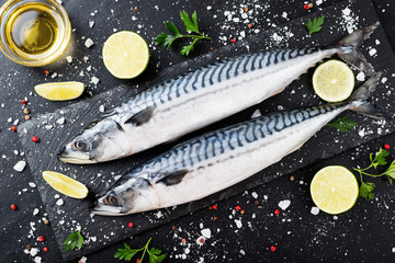 Fresh fish. Mackerel with salt, lemon and spices on black stone background. 