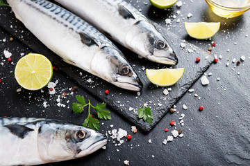 Fresh fish. Mackerel with salt, lemon and spices on black stone background. 