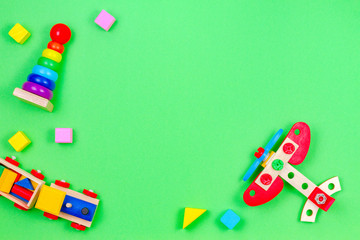 Baby kids toys background frame with wooden train, plane, baby stacking rings pyramid and colorful blocks on green background