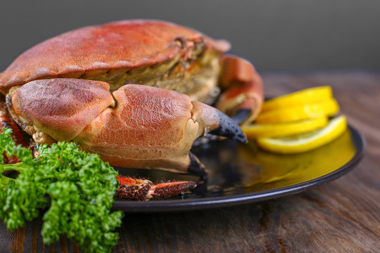 Cooked crabs on black plate served with fresh lemon and parsley, wooden background, top view.