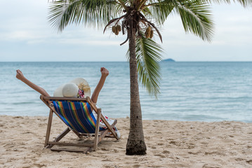 Summer beach vacation concept, Happy young Asian woman with hat relaxing on beach chair and raised arms up.