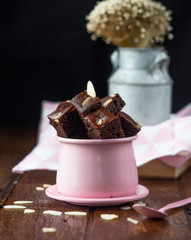 Piece of brownie almond in pink cup with pink spoon and dry flower on wood table.