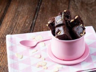 Piece of brownie almond in pink cup with pink spoon and dry flower on wood table.