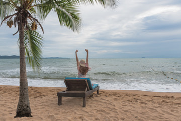 Summer beach vacation concept, Happy young Asian woman with hat relaxing on beach chair and raised hands up.