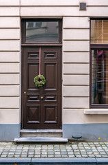 Vintage brown front door decorated with Christmas wreath shot in Bruges, Belgium. Old brown door with window at the top.