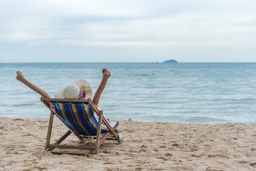 Summer beach vacation concept, Happy young Asian woman with hat relaxing on beach chair and raised hands up.