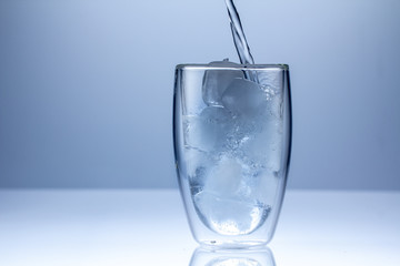Pouring water into glass on blue background close up