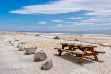 Obraz premium Wooden picnic table on a white sand beach at a lake side