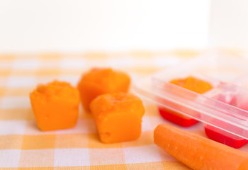 Preparing baby food, homemade. Frozen carrot made as an ice cube on yellow cutting board. Healthy food kids concept. Selective focus.