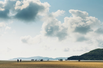 Landscape of low tide with green mountain, cloud sky with people in background at Toong Pronge Bay in Chon Buri, Sattahip District, Thailand.