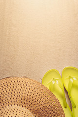 Summer holiday background with yellow flip flops and straw hat on sandy beach, top view with copy space