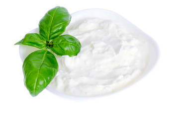 Ceramic bowl with white natural yogurt and green basil leaves.