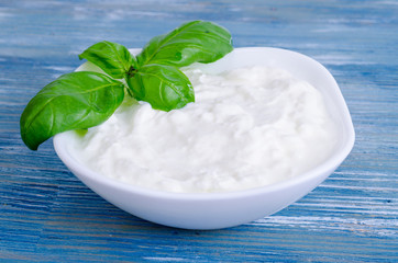 Ceramic bowl with white natural yogurt and green basil leaves.