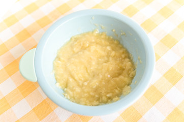 Preparing baby food, homemade.Top view of a bowl with smashed banana mixed with breast milk in a blue bowl on a tablecloth. Healthy food kids concept. Selective focus.