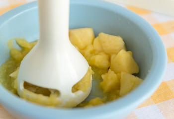 Chopping and mixing boiled or stewed apples in a bowl with mixer. Preparing baby food, homemade....