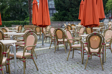 Empty outdoor cafe with closed umbrellas. Street cafe with empty tables and chairs. Restaurant furniture concept. European cafe in summer patio. Summer terrace with tables and free seats. 