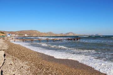 Empty pebble beach in Koktebel in the Crimea in mid-October. In the clear sunny weather, small waves runs onto the shore. Sea and ocean, nature, travel and tourism concept.
