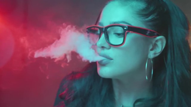 Gorgeous brunette woman smoking electronic cigarette in neon color light - video in slow motion