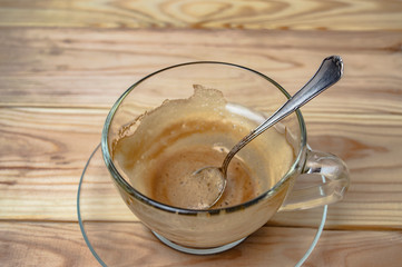 empty cup of espresso and a silver coffee spoon on a wooden table close up