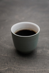 A vertical low key photo of a green cup of black coffee on a wooden table