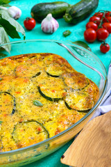 Zucchini, cheese, eggs, cream and green casserole in a transparent glass form on a bright background. Tasty healthy dish.