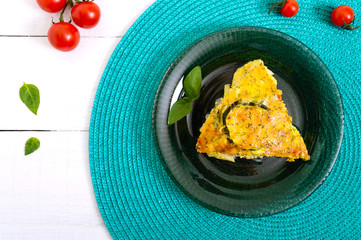 Zucchini, cheese, eggs, cream and greens casserole on a white wooden background. Portion of casserole on a plate. Tasty healthy dish. Top view, flat lay.