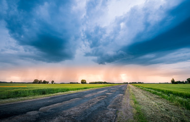 Impressive thunderstorm over a barley field in summer time. Dark storm clouds covering the rural landscape. Intense rain shower in distance. Motion created by windy weather. 