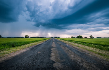 Impressive thunderstorm over a barley field in summer time. Dark storm clouds covering the rural landscape. Intense rain shower in distance. Motion created by windy weather. 