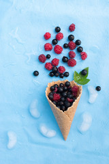 Ripe summer berries - currants, blueberries, raspberries in a waffle cone on a blue background with ice. View from above. Banner. Template for minimal style. Pop art design, creative concept