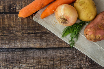 Young raw unpeeled potatoes, onions,  carrots and bunches green on  dark wooden background. Harvest, vegetables. Flat lay composition. Layout with copy space for text.