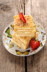 Napoleon cake dessert decorated with strawberries on a beautiful plate on an old wooden background