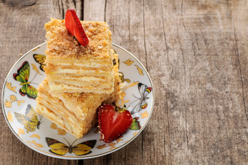 Napoleon cake dessert decorated with strawberries on a beautiful plate on an old wooden background