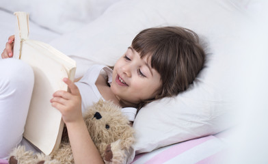 Cute little girl smiling while lying in a cozy white bed