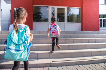 Back to school education concept with girl kids, elementary students, carrying backpacks going to class