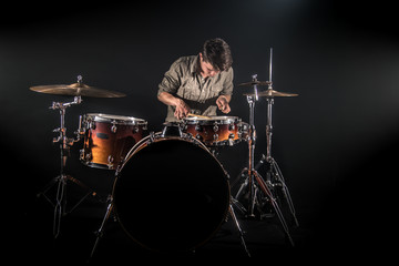 Professional drummer playing on drum set on stage on the black background